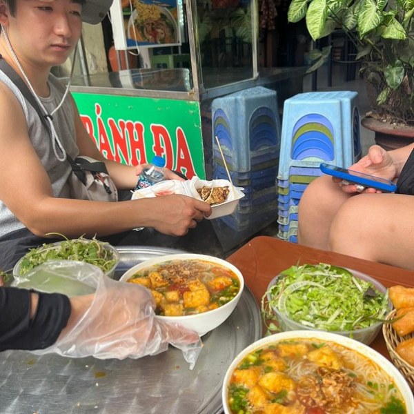 People enjoying noodle soup and salad at a street food stall.