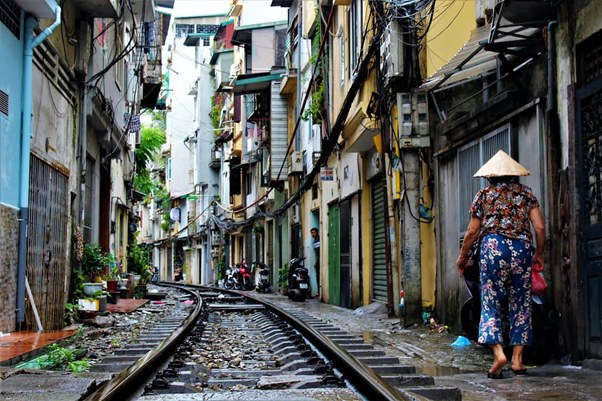 Narrow street with train tracks, lined by buildings and a walking person in a conical hat.
