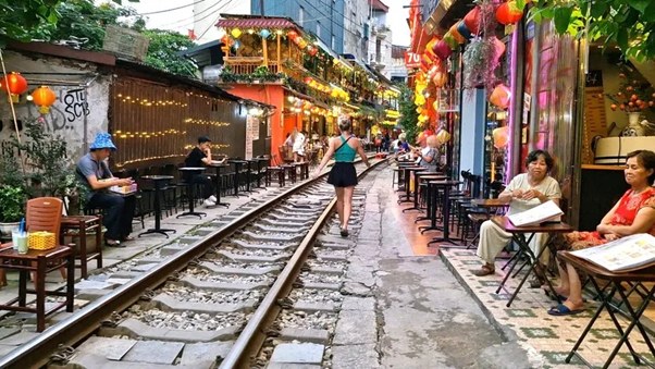 People sitting at outdoor cafes along a narrow railway track lined with colorful lanterns.
