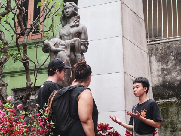 Three people conversing near a statue in an urban setting.