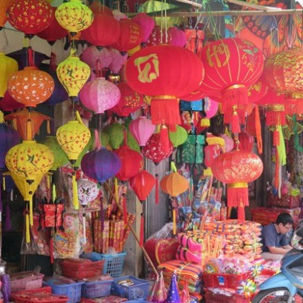 Colorful lanterns hanging in a busy market stall filled with festive decorations.