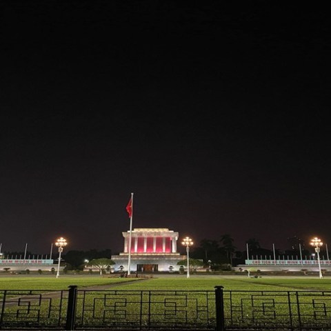 Illuminated mausoleum and flag at night, with a dark sky and lights.