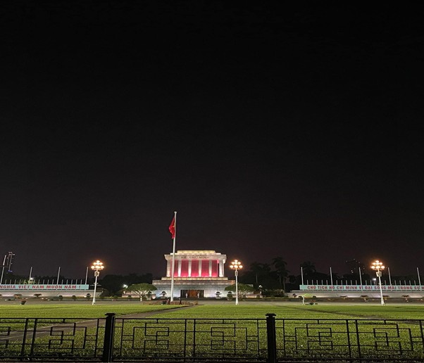 Illuminated mausoleum and flag at night, with a dark sky and lights.