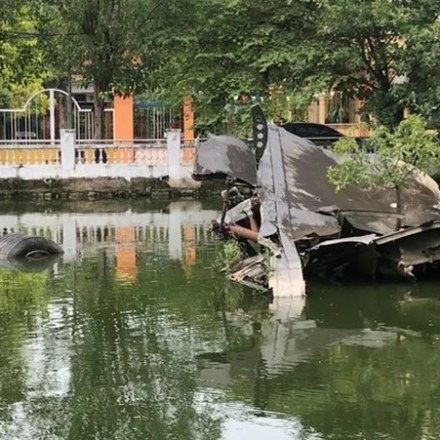 Wreckage of an aircraft submerged in a pond with trees in the background.