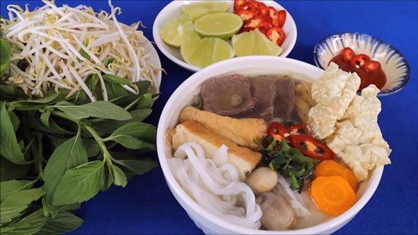 Vietnamese noodle soup with herbs, lime, and chili on a blue background.