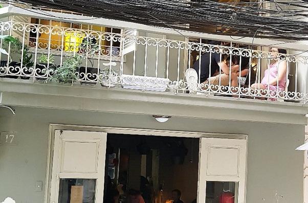 People sitting on a balcony above a cafe, with plants and railing.
