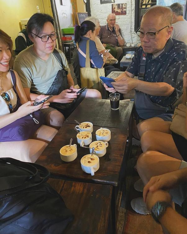 People sitting around a table with cups of coffee, using phones in a cozy cafe.