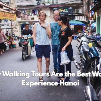 Three people walking on a narrow street in Hanoi with motorbikes and text overlay about walking tours.