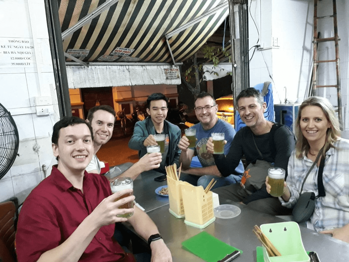 Group of six people smiling and toasting with drinks at a table.