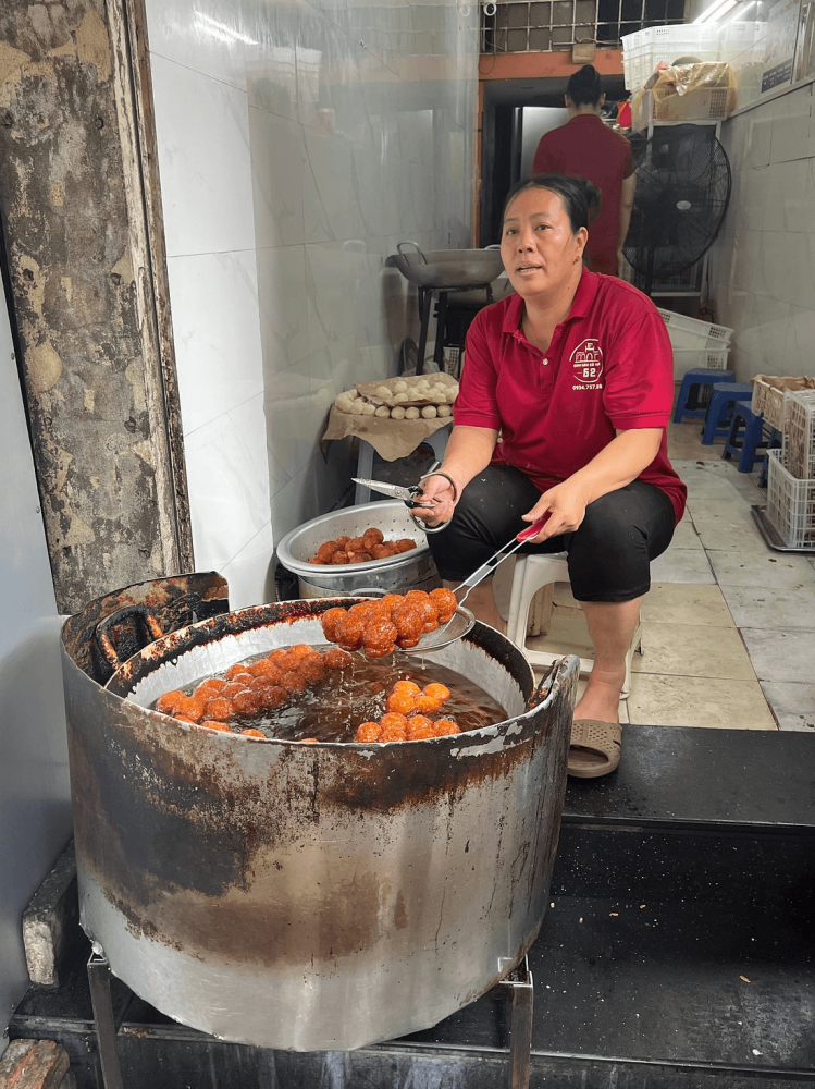 Woman frying snacks in a large pot on a street.