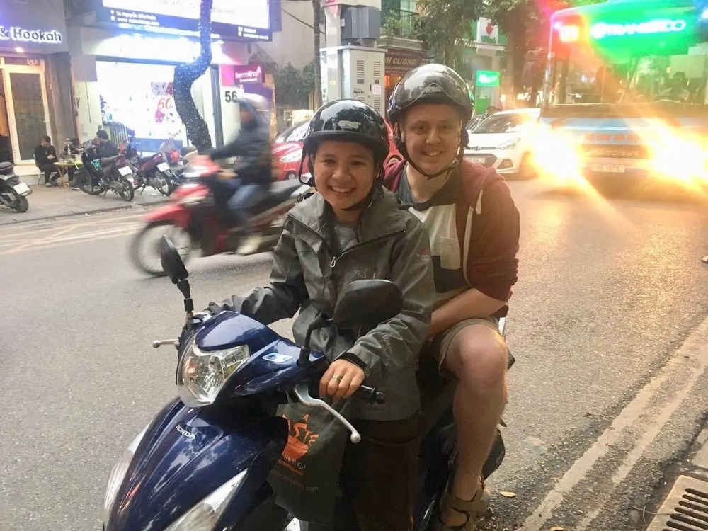 Two people on a scooter in a busy street with helmets.