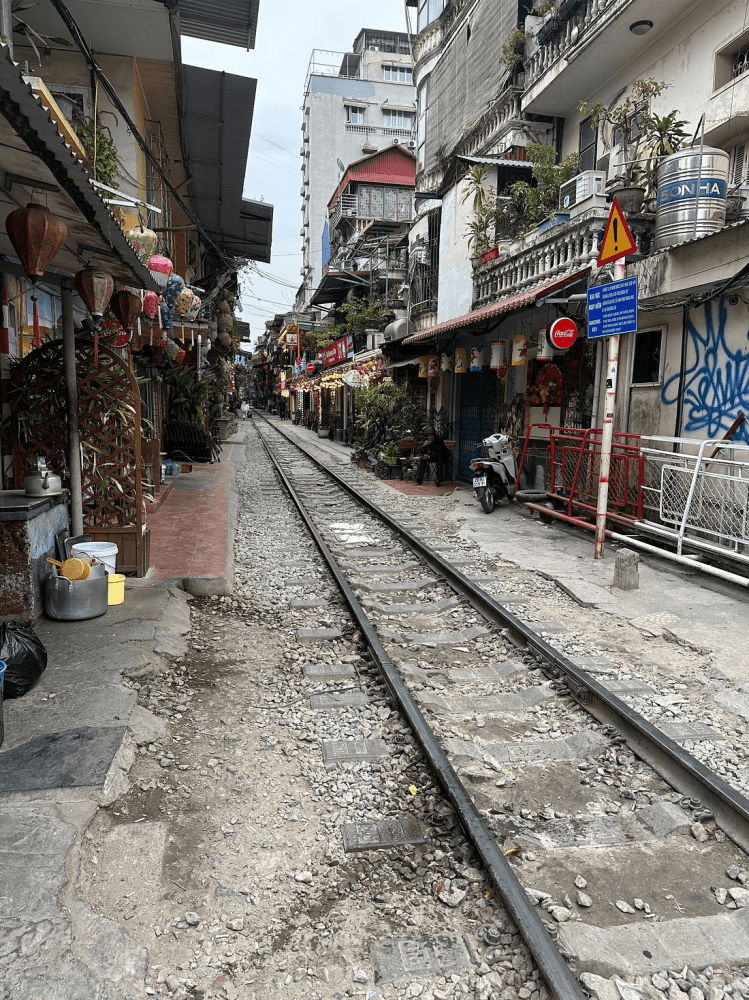 Narrow urban street with railway tracks and buildings on both sides.