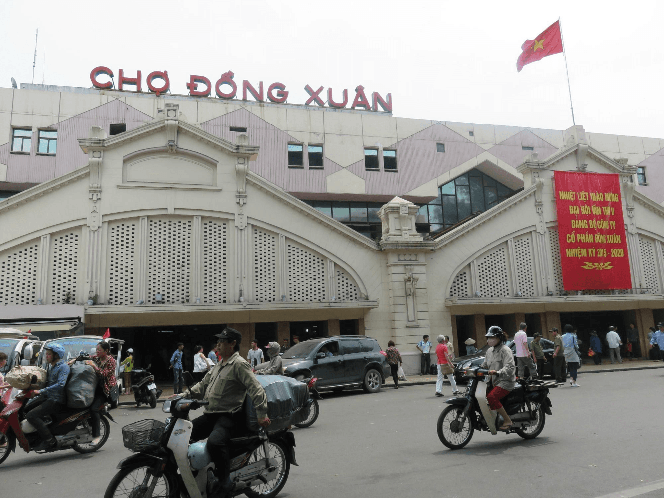 Busy street scene in front of Cho Dong Xuan market with motorcycles and people.