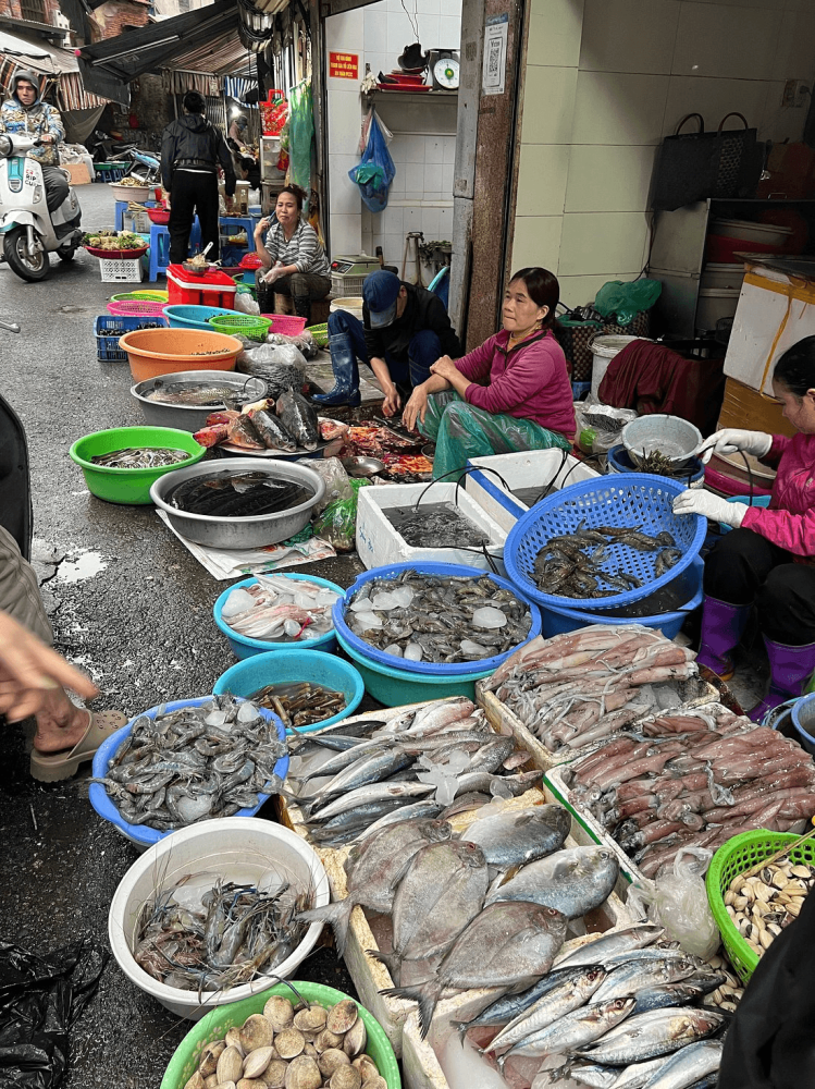 Street market with vendors selling various seafood items in bowls and baskets.