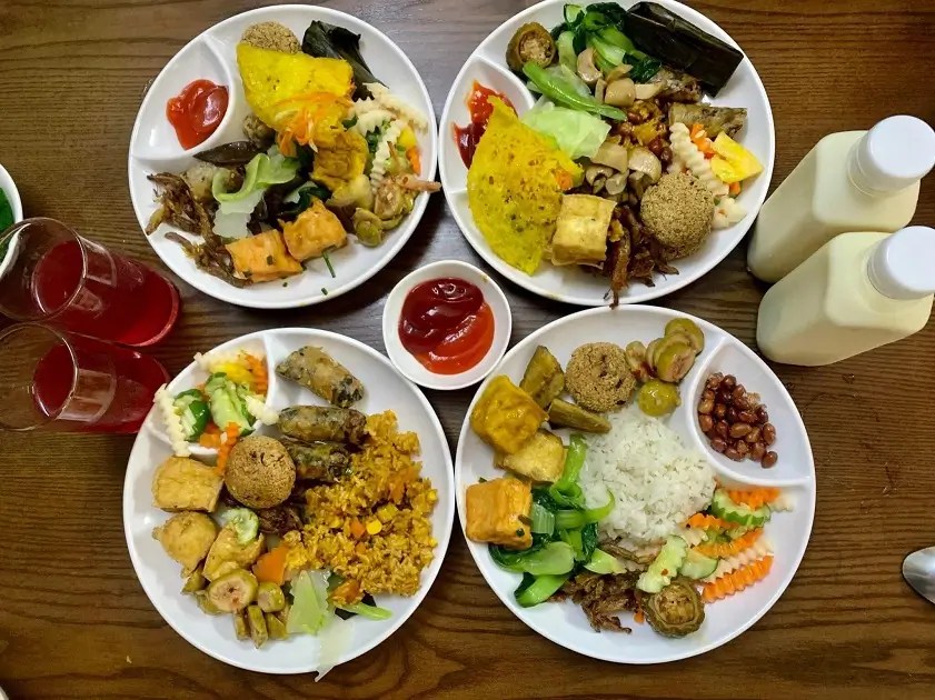 Four plates of assorted dishes with drinks and condiments on a table.